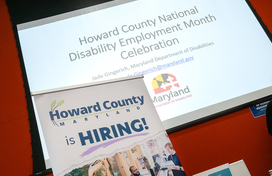A photo of a project screen that reads Howard County National Disability Employment Month Celebration with a pop up sign in front of it that reads Howard County is hiring.