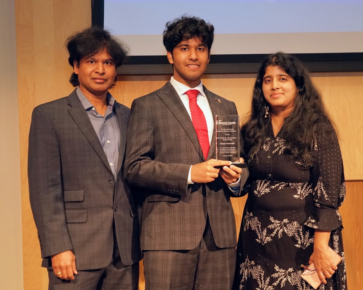 Three people in business formal dress. The person in the center holds a clear glass award. 