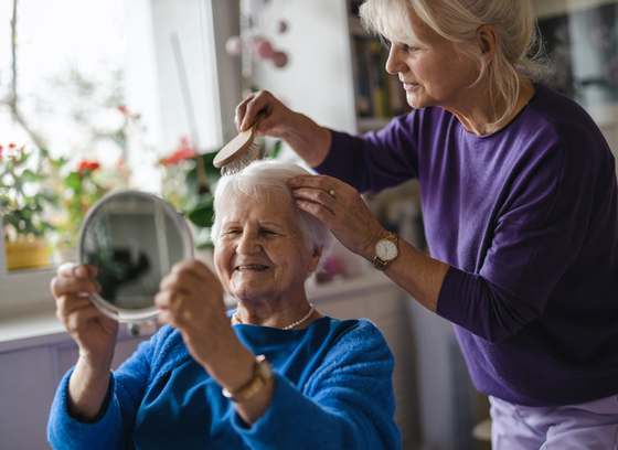 A person brushes an older adult's hair