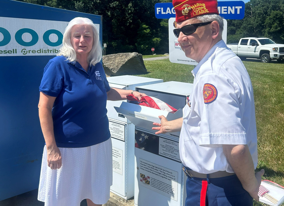 A woman places a flag in the flag retirement container at the Alhpa Ridge Landfill as a veteran looks on.